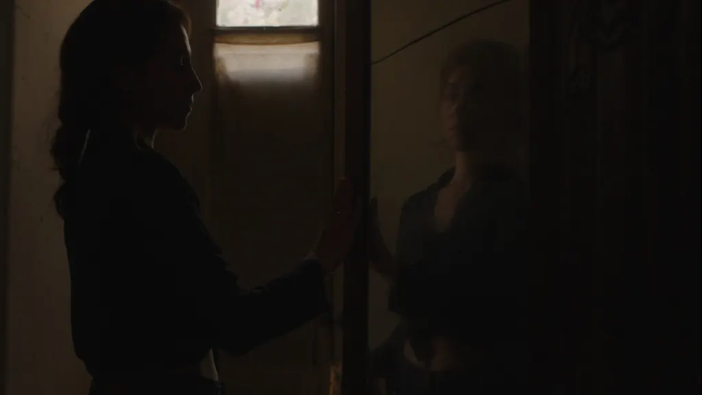 Joanna Kalafatis in silhouette, her hand on a mirror, her reflection facing her