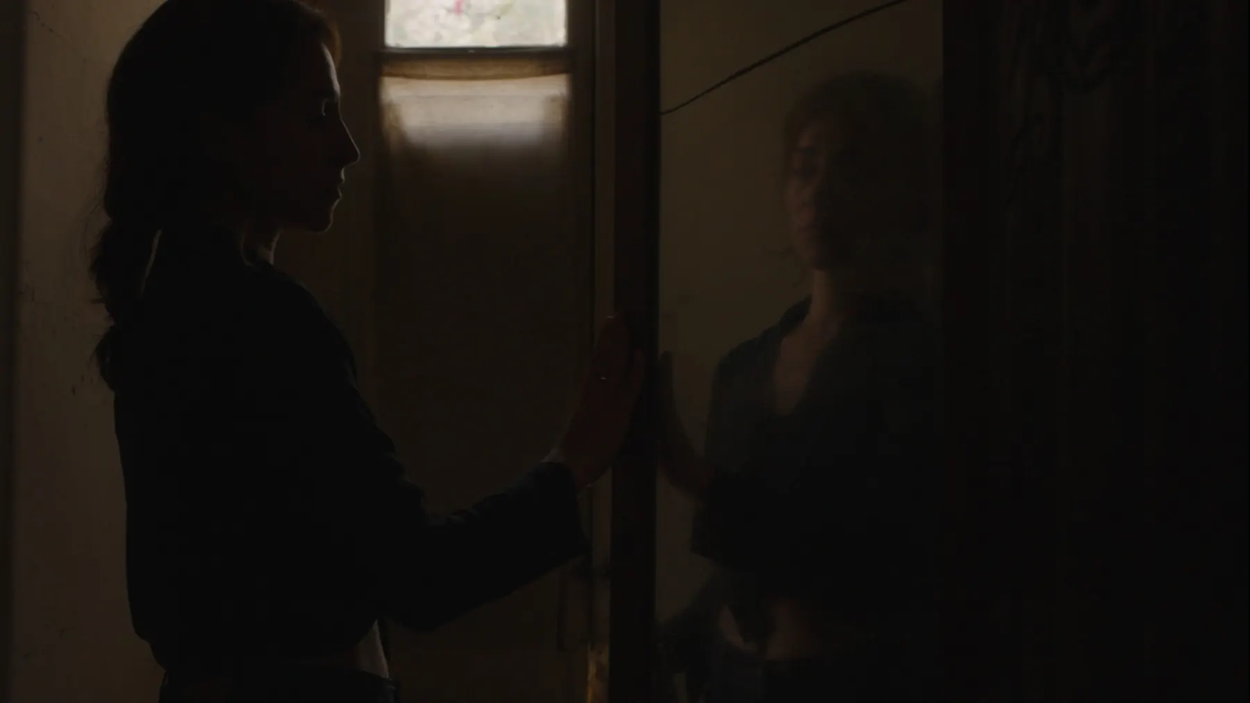 Joanna Kalafatis in silhouette, her hand on a mirror, her reflection facing her