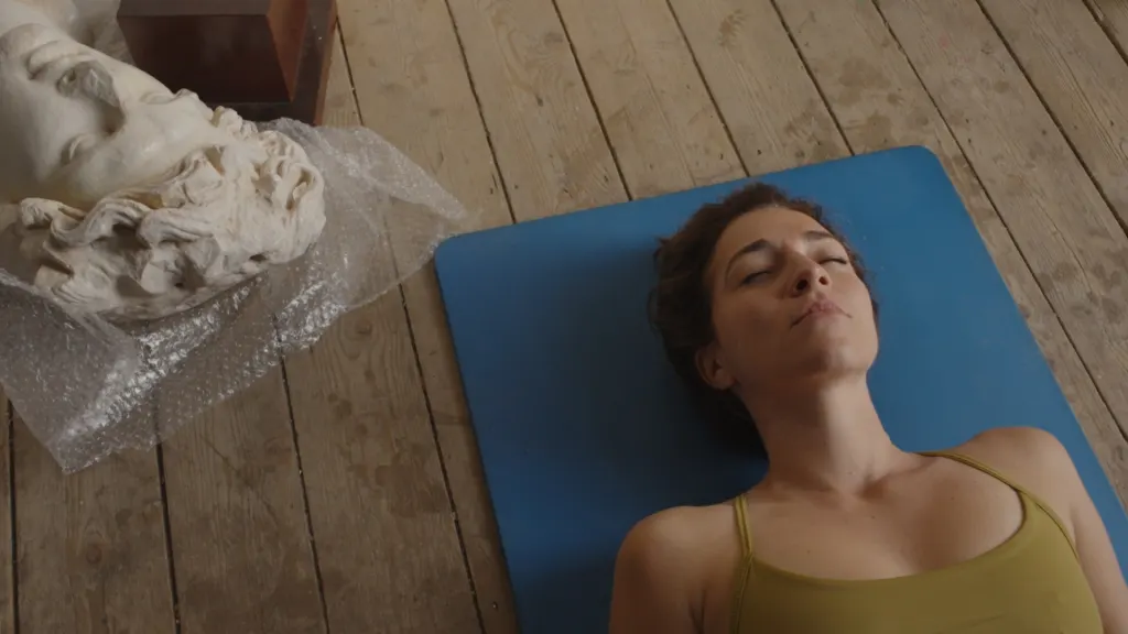 Joanna Kalafatis lying on a blue mat beside a marble head wrapped in bubble wrap